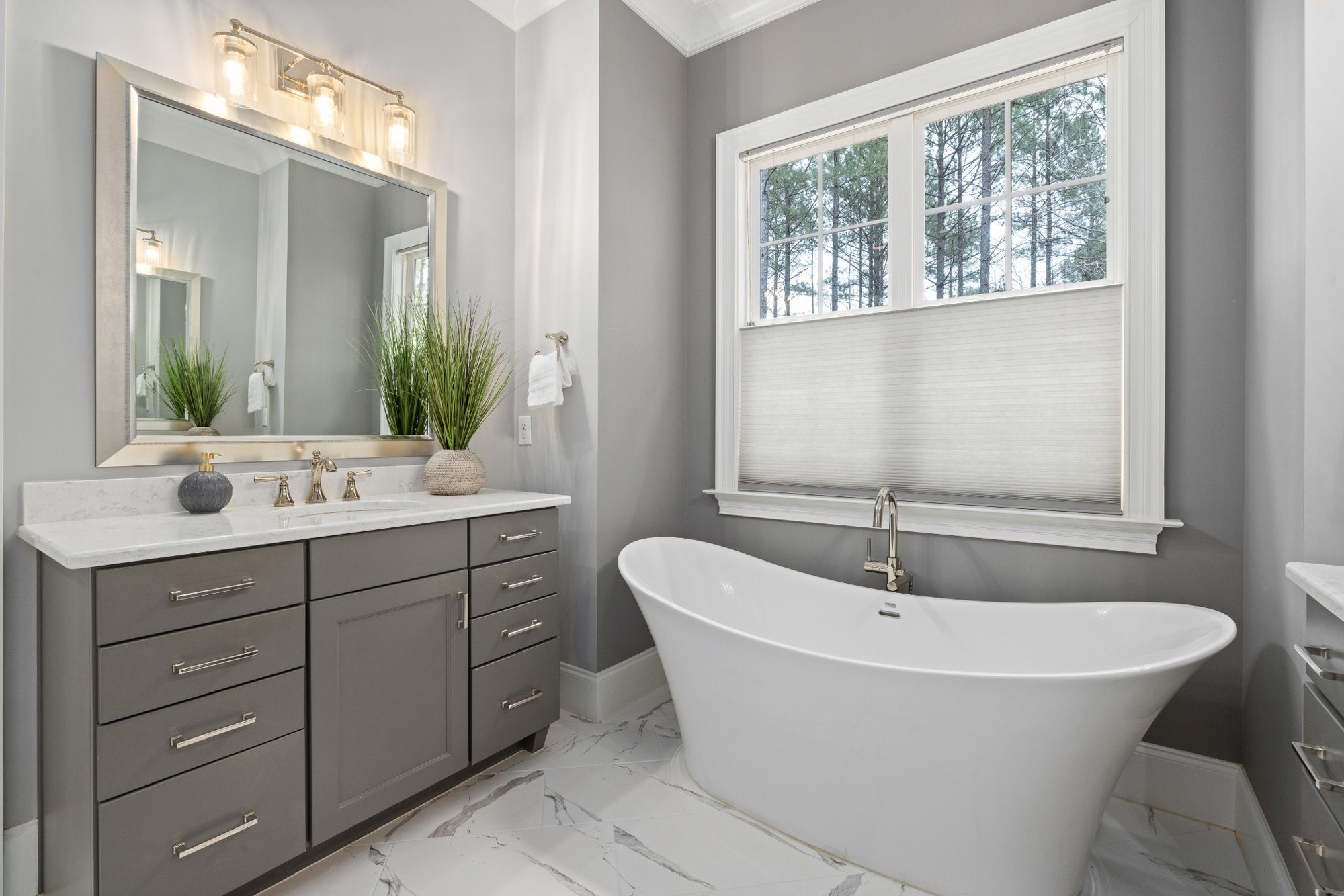 Stock image of modern bathroom with freestanding tub, gray vanity, marble tile floor, and large window -optimized