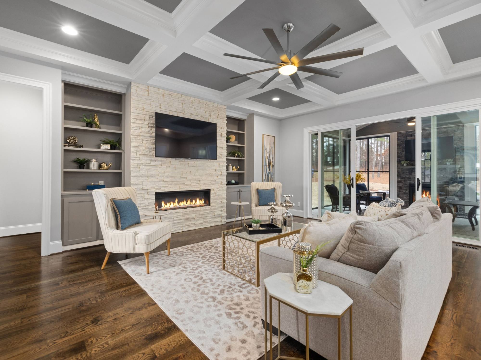 Stock image of a living room with stone fireplace, built-in shelving, coffered ceiling, and sliding doors in Northern California - optimized