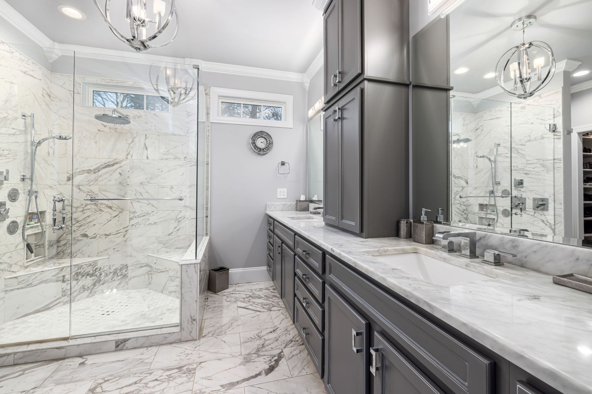 Stock image of luxury bathroom with marble walk-in shower, dark gray vanity, and marble countertops -optimized