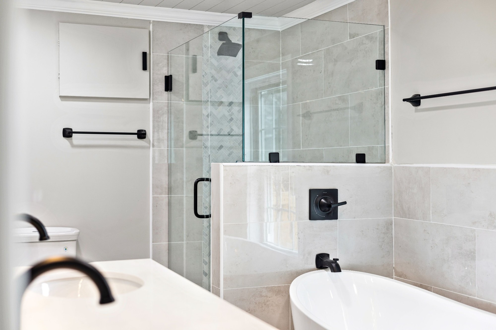 Stock image of modern bathroom with glass shower, soaking tub, gray tile, and matte black fixtures -optimized