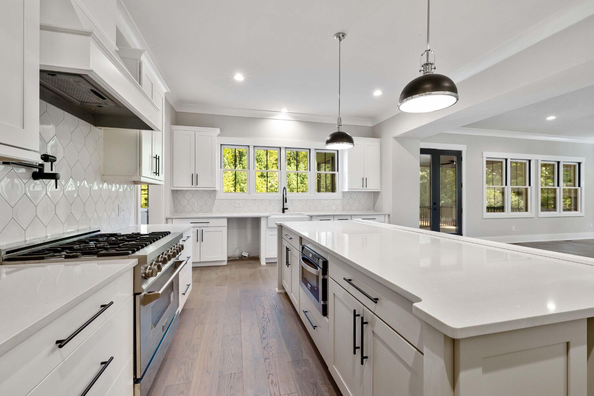Stock image of modern white kitchen with quartz island, black pendant lights, and wood floors northern california -optimized