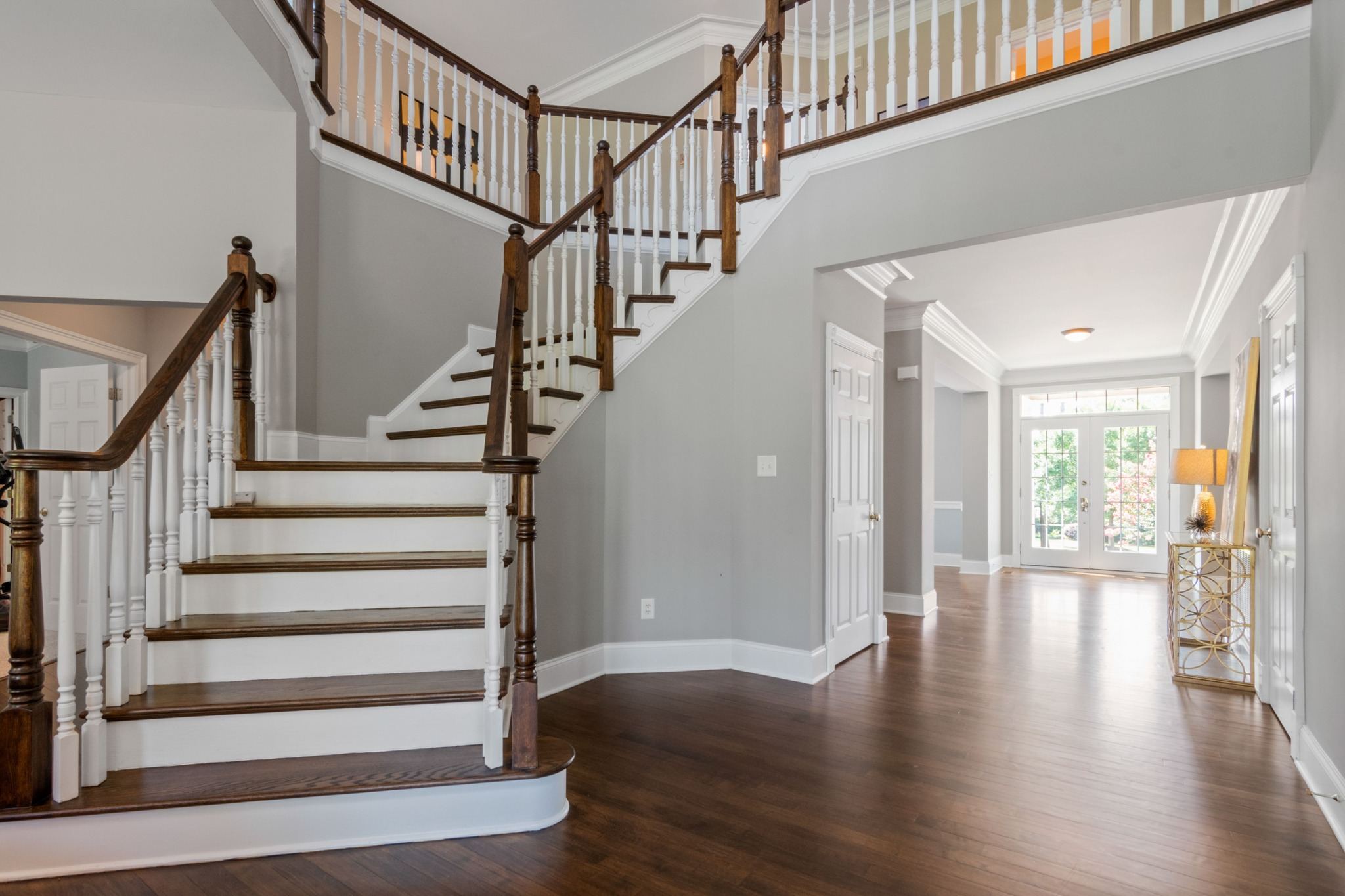 Stock image of a bright foyer with hardwood staircase, white spindles, and open hallway in Northern California -optimized